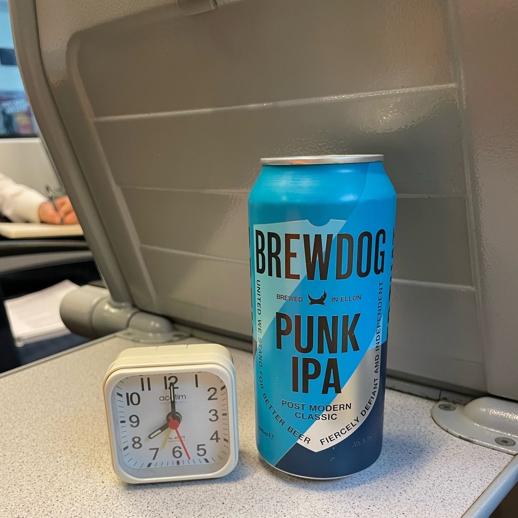 photo of a small travel alarm clock next to a can of brewdog punk IPA on a train travelling from Winchester to Southampton