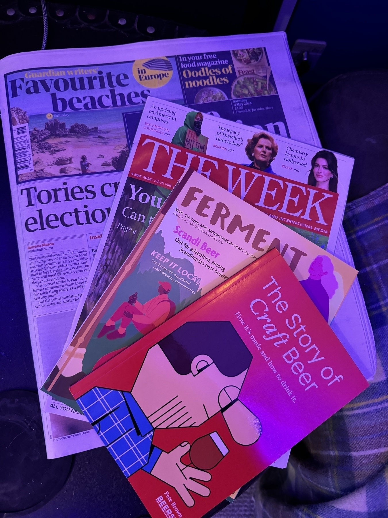 a stack of Adams paper based subscriptions on a table, The Saturday Guardian UK paper, the week UK magazine, a book on the story of craft beer from beer52 and a beer52 magazine on Scandinavian beers