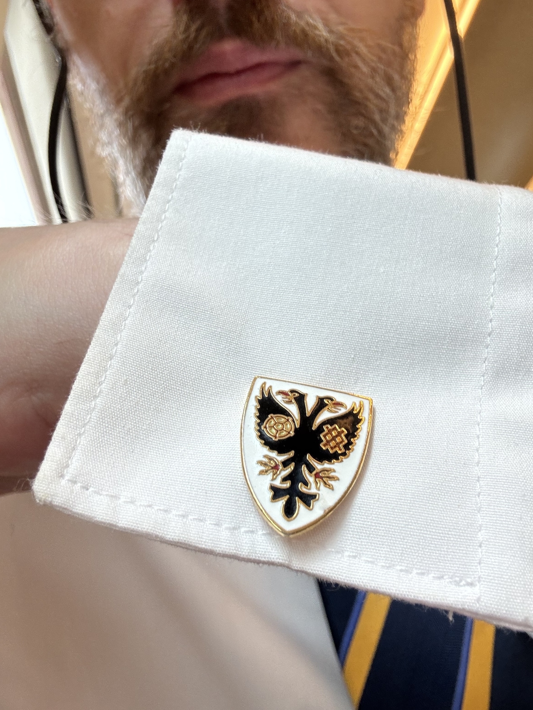 Adam is wearing a white shirt with a unique cufflink in the shape of the crest of AFC Wimbledon.