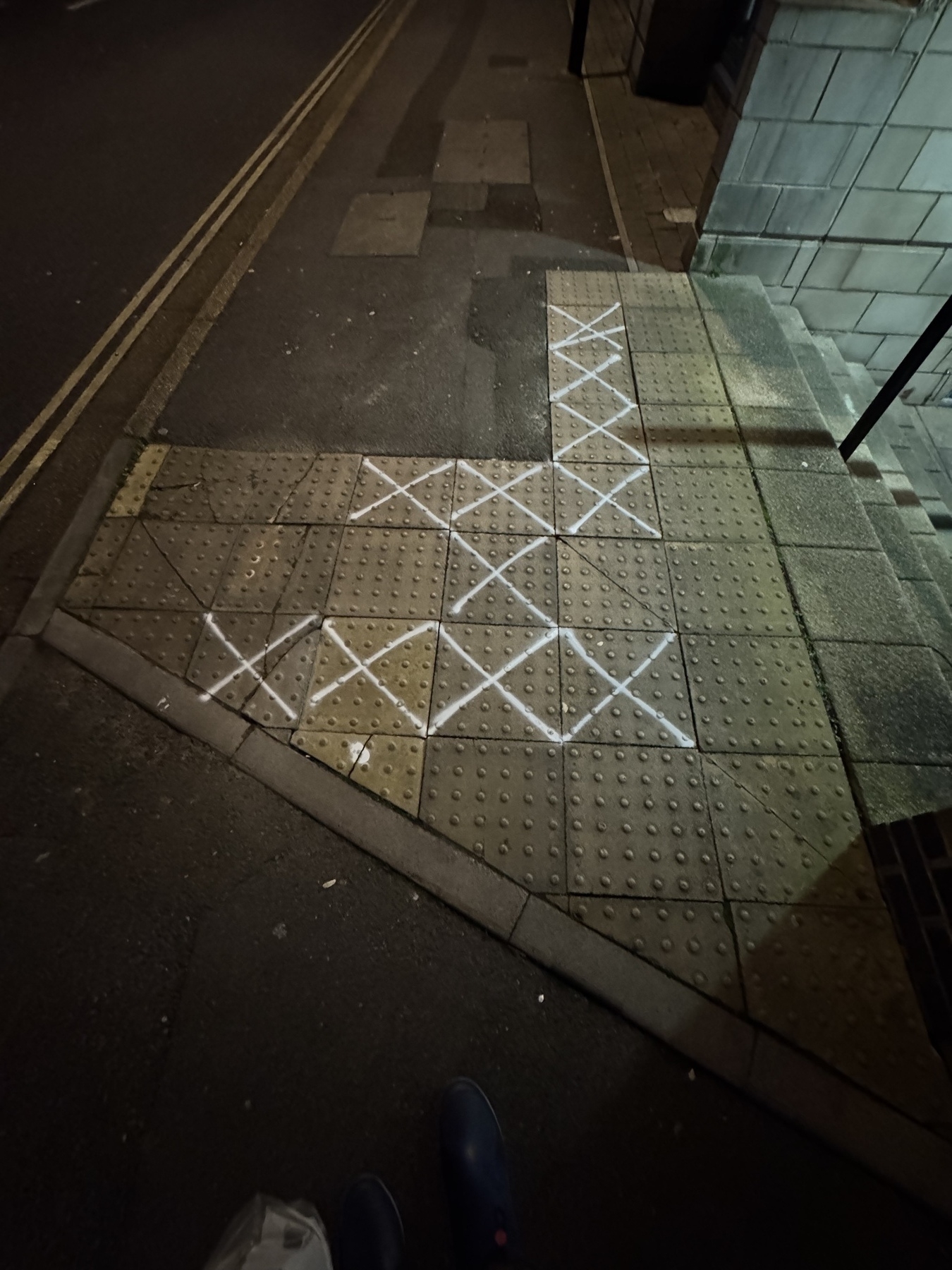 Image of a pavement in Southampton made up of individual concrete squares with the ones that are wobbly to walk on marked with a spray painted X 