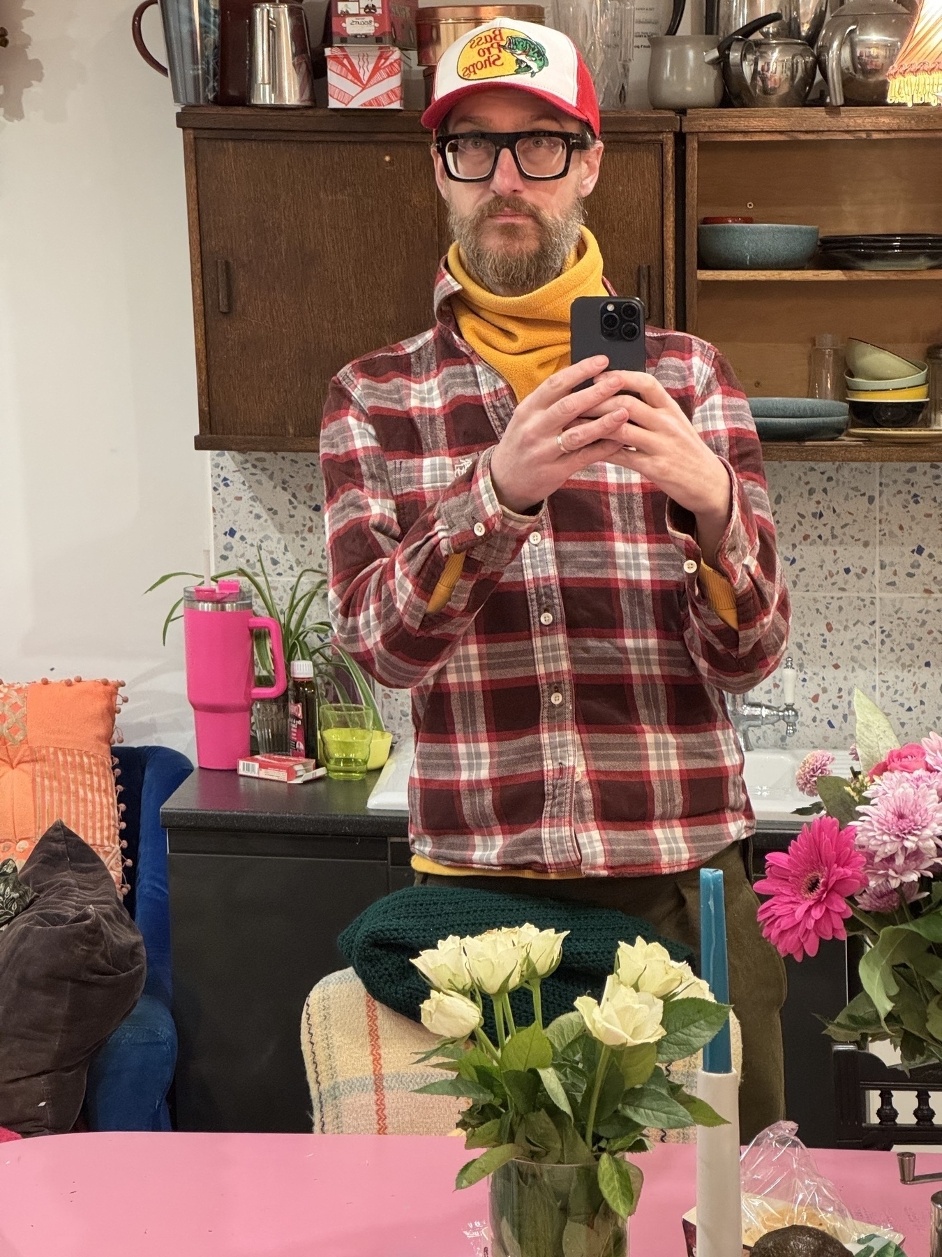 A photo of myself looking into a mirror wearing my new big framed glasses, my new pro bass shop baseball cap a yellow snood and tamed and white lumberjack style jacket