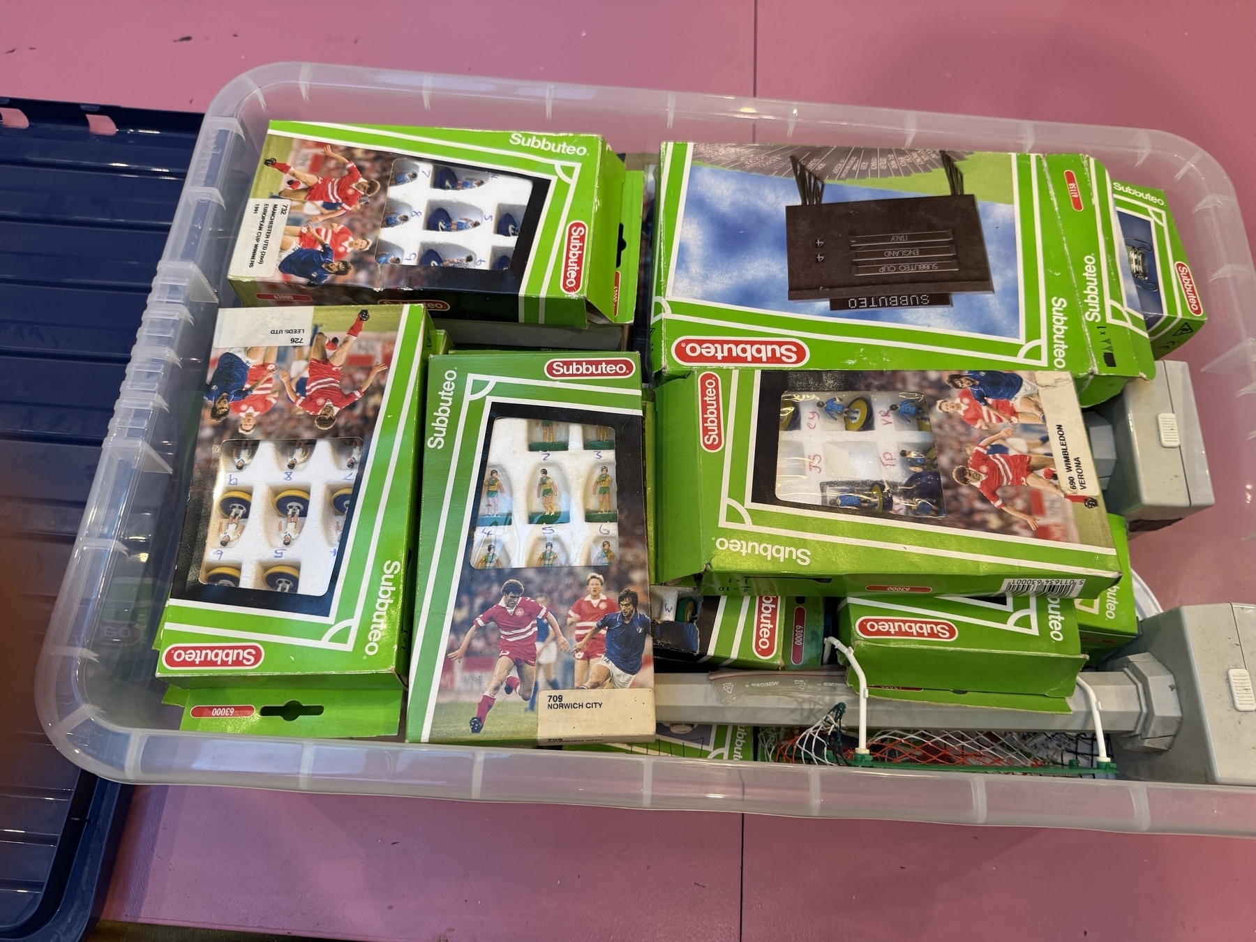 A plastic bin is filled with several boxed sets of Subbuteo, a tabletop sports game.
