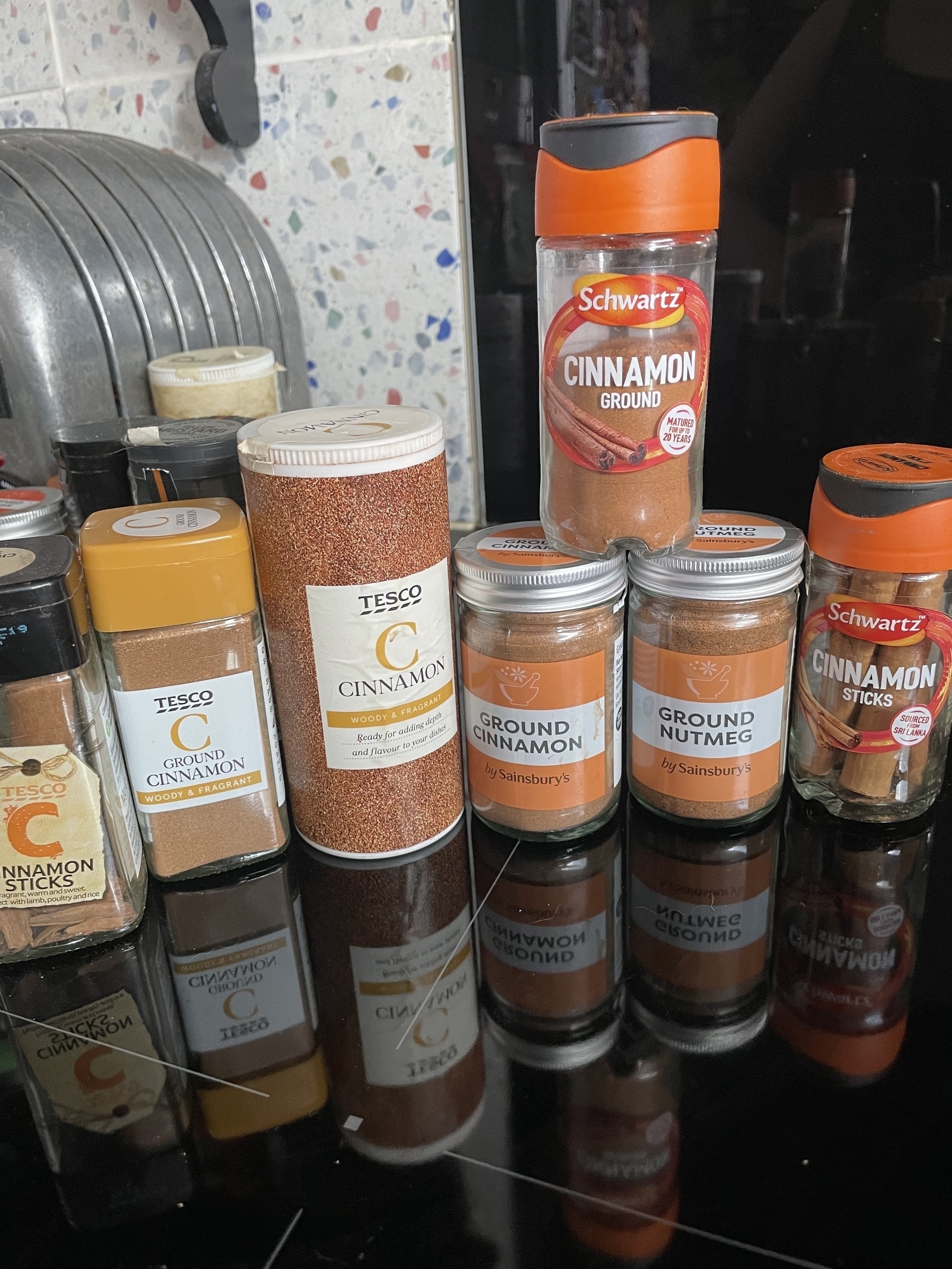 A collection of various cinnamon spice containers is displayed on a reflective surface.
