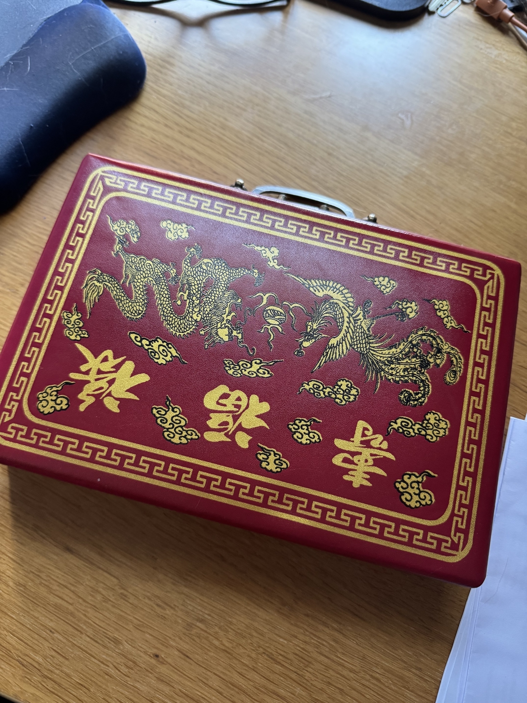 A red Mahjong case featuring gold dragon designs and Chinese characters sits on a wooden desk.