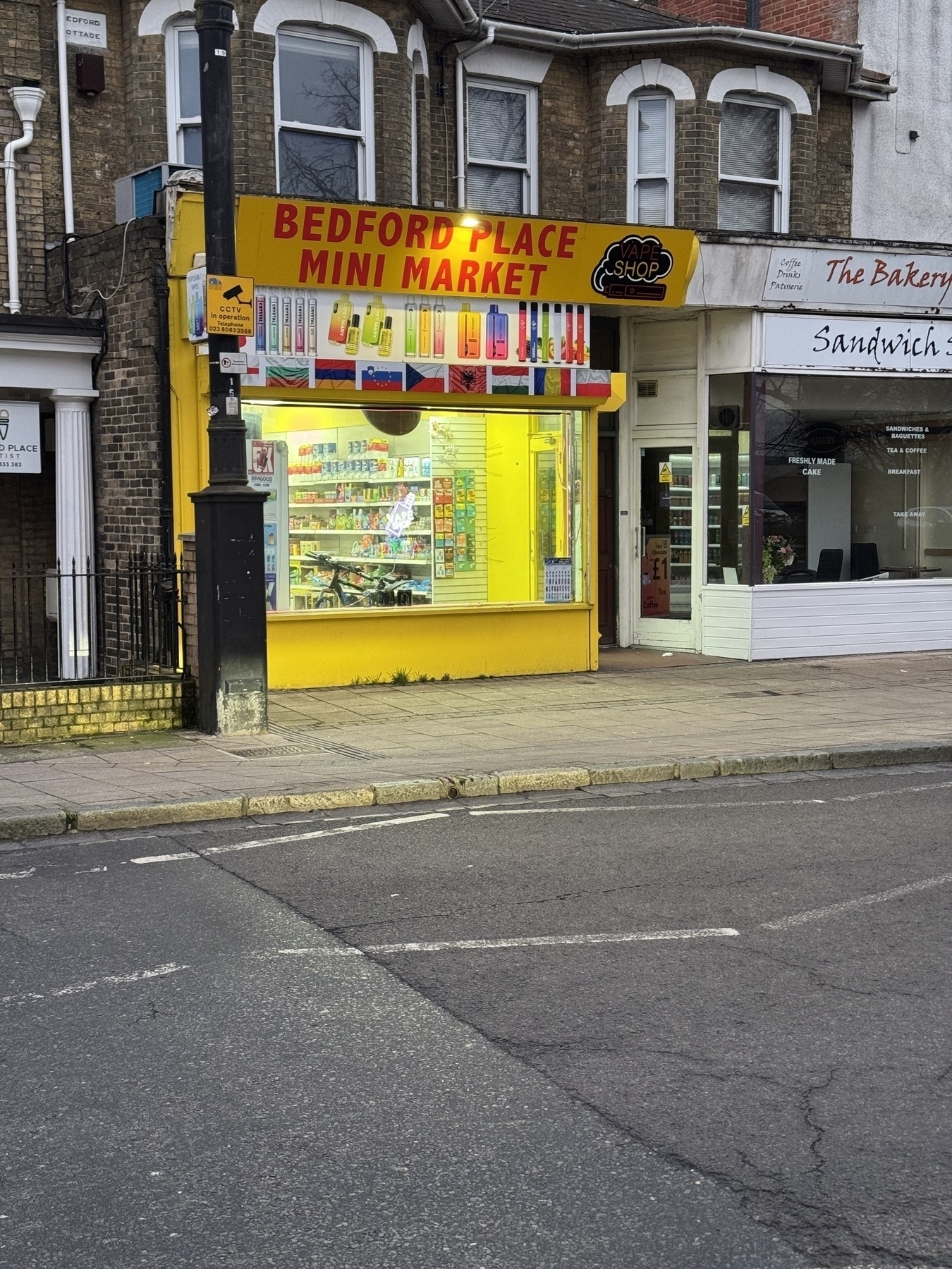 Photo of a shop light up and painted yellow. The sign says mini market but everything in the window and visible is a vape
