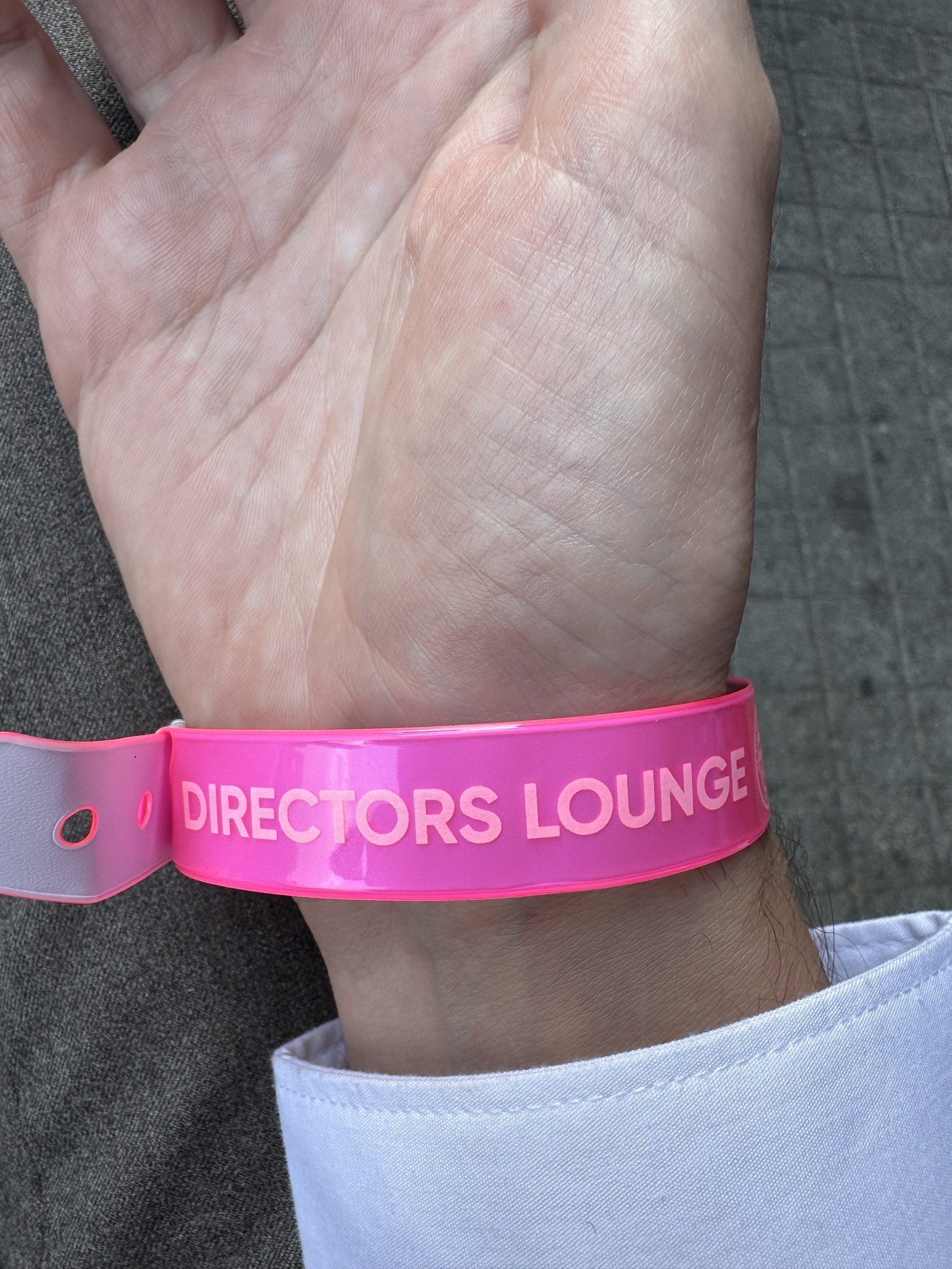 A pink wristband labeled "DIRECTORS LOUNGE" is worn on a person's wrist.