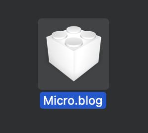 A 3D white cube resembling a building block is displayed above the text "Micro.blog" on a dark background.