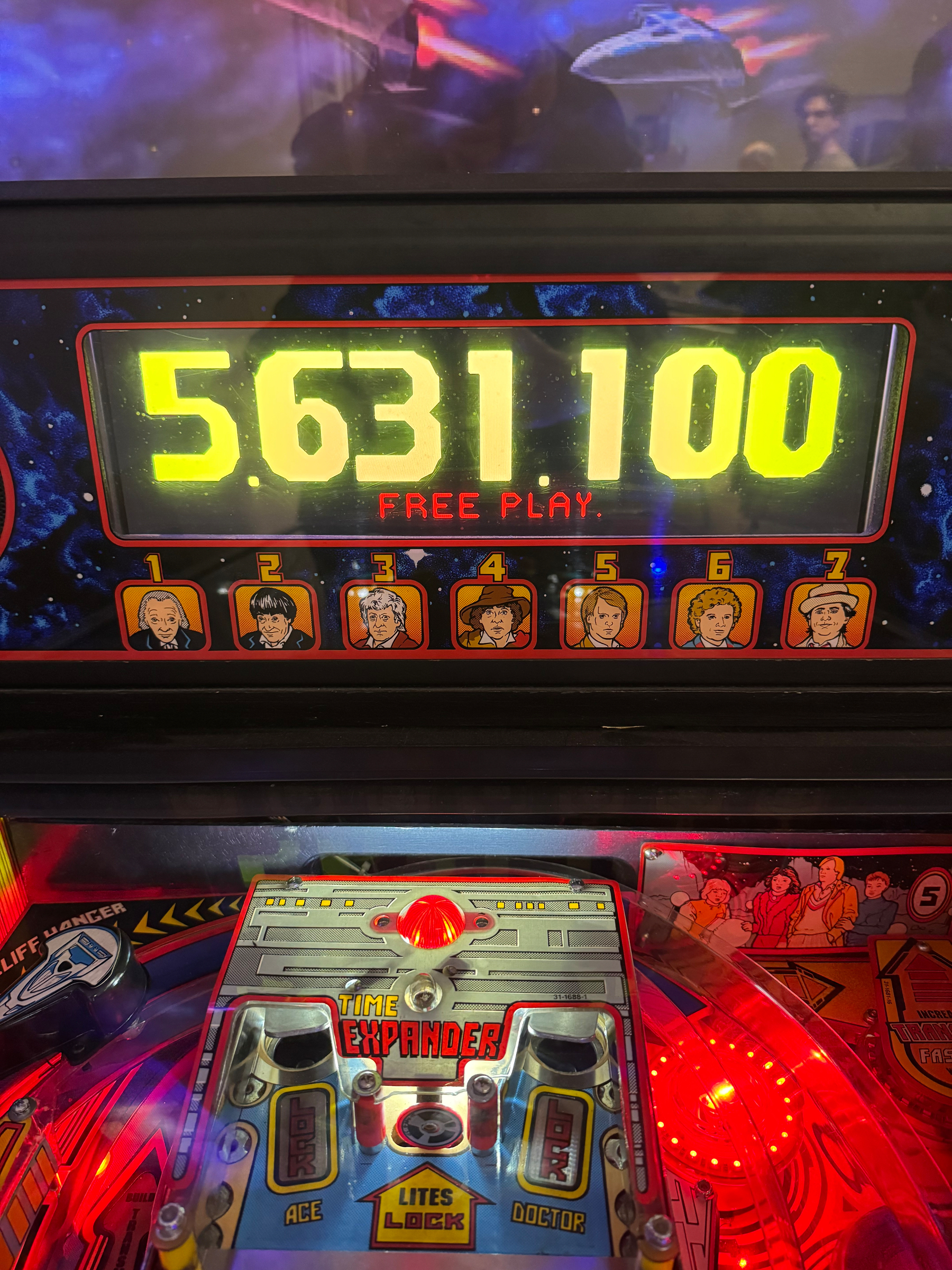 A pinball machine display shows a score of 5,631,100 with the text FREE PLAY and includes comic-style illustrations of seven characters.