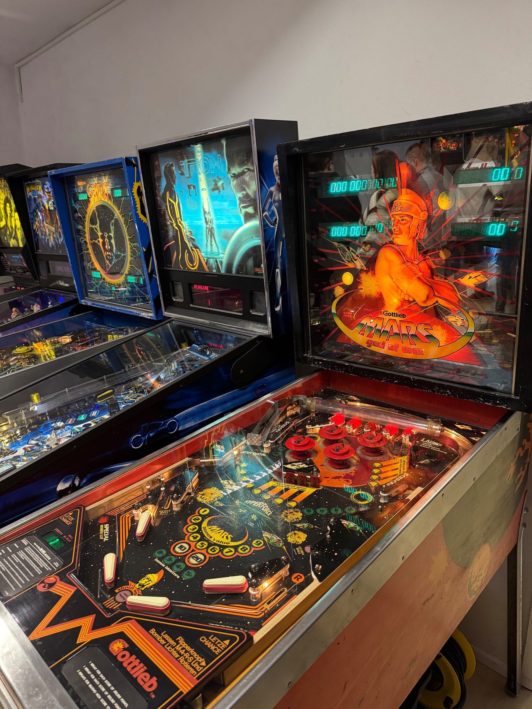 A row of vintage pinball machines is set up against a wall in an arcade.