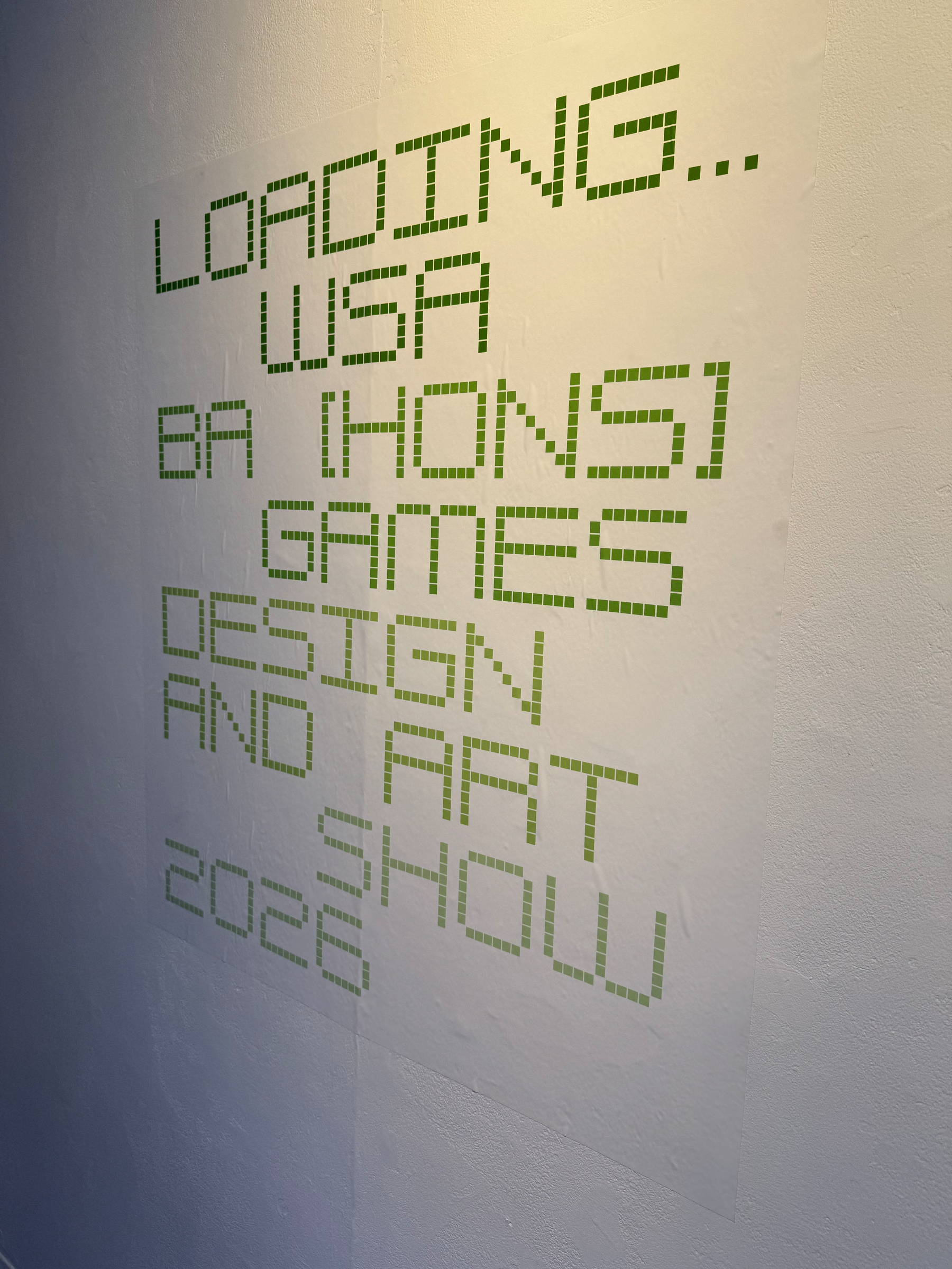 Text on a wall reads LOADING... WSA BA (HONS) GAMES DESIGN AND ART SHOW 2023 in a pixelated font.