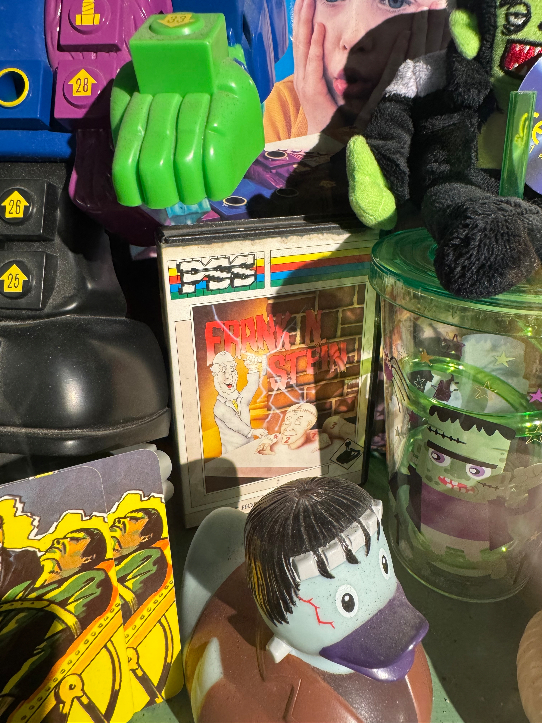 A collection of Halloween-themed toys and decorations, including a Frankenstein-themed rubber duck and a horror story box, is displayed on a shelf.